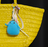 Frimousse petite poupée  de forme ronde de couleur bleu  crochetée en fil de coton à la main à bali dans un atelier artisanal accompagner de rubans imprimés de mots bienveillants accroché à un panier en osier de coloris jaune  @lesfelicites Les Félicités 